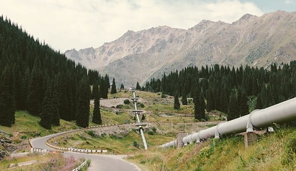 Pipeline running through a mountain valley with forests and winding roads, supporting energy infrastructure.